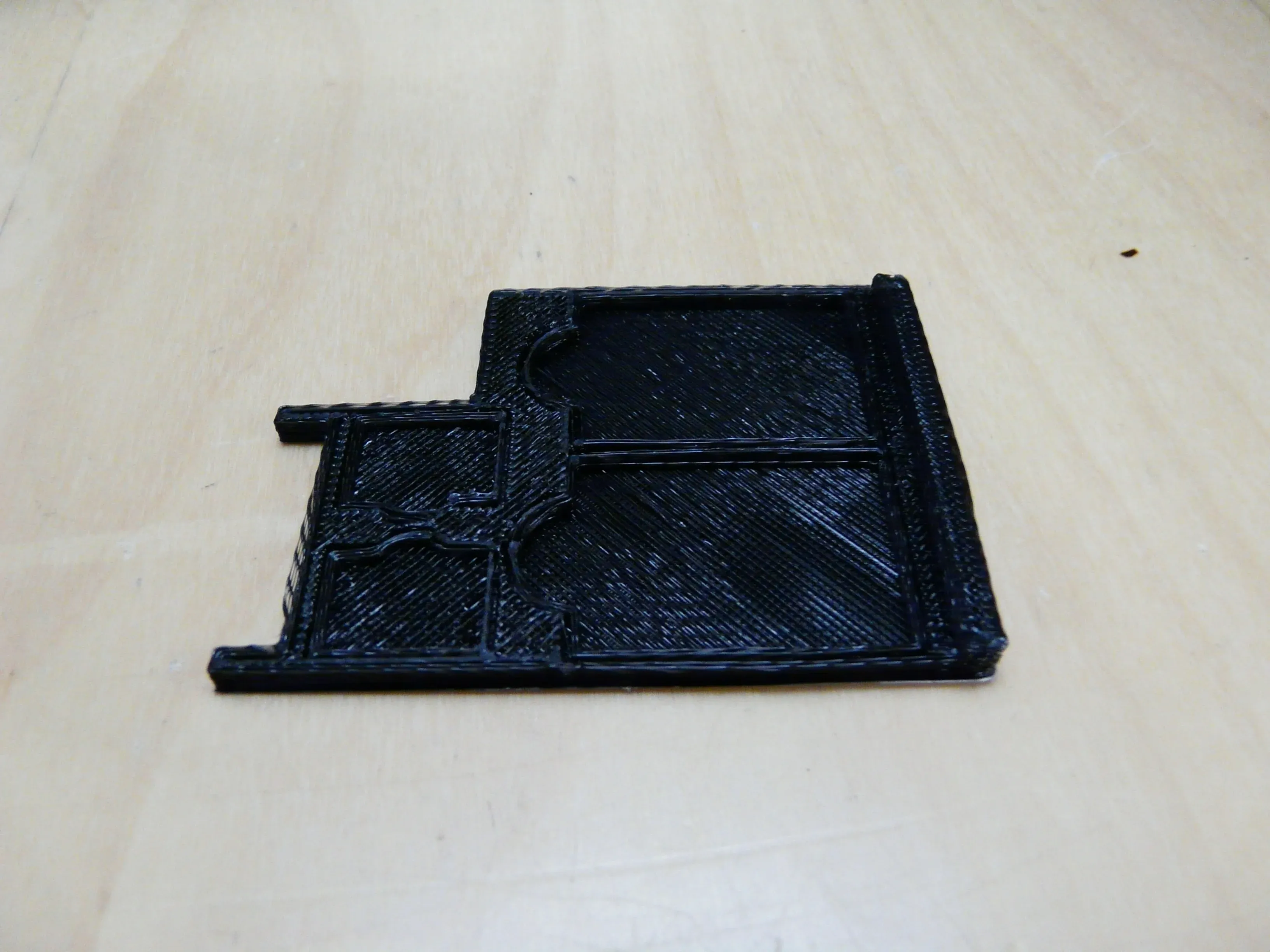 Musta litteä 3D-tulostettu suojakappale vaalealla pöydällä.