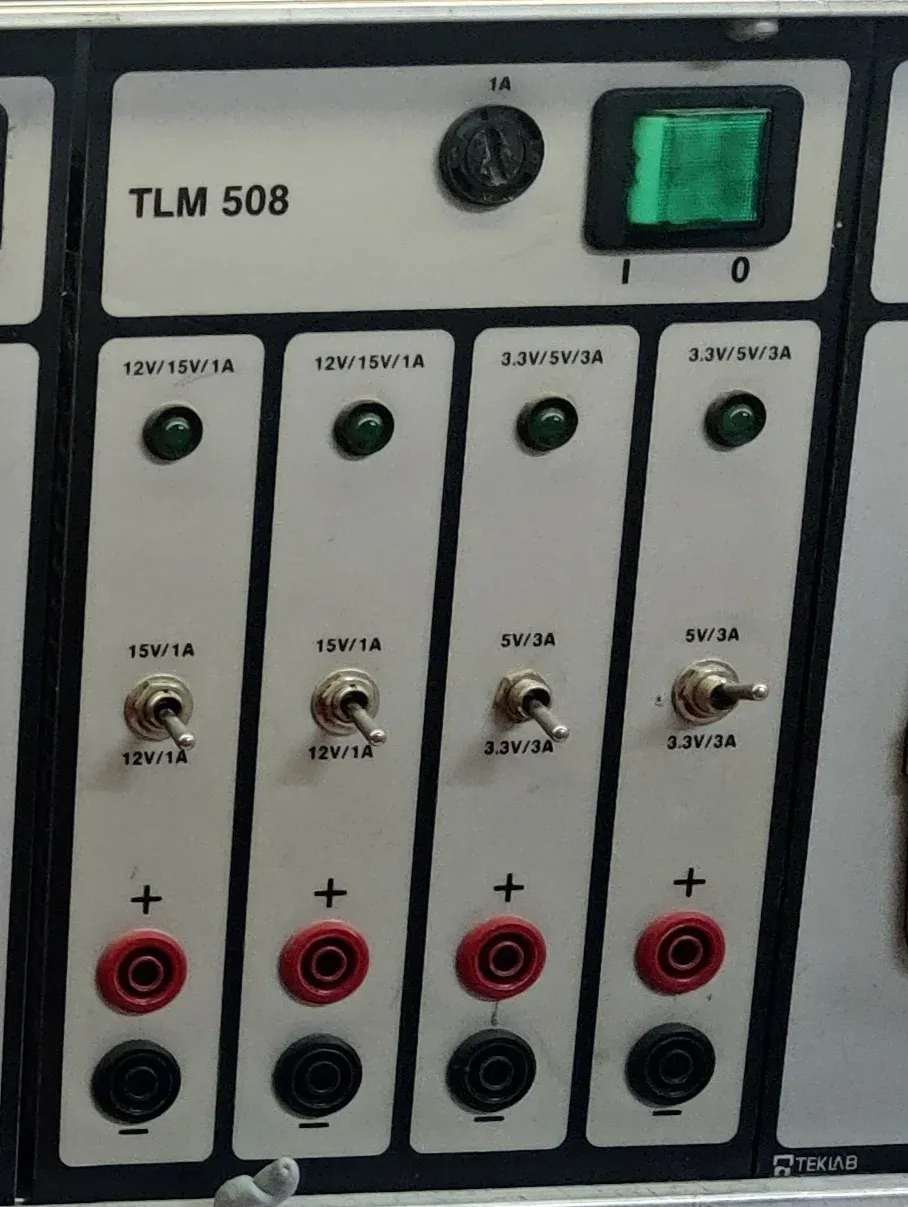 Elektroniikkapöytään integroitu TLM 508 -virtalähde, jossa näkyvät neljä valittavaa lähtöä sekä niiden jännite- ja virtamerkinnät.